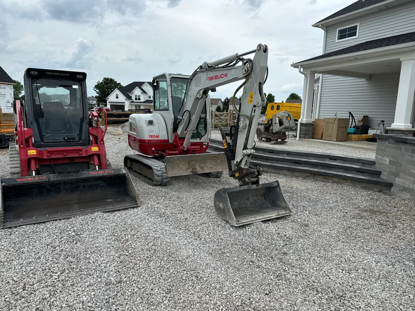 Two compact excavators staged on a gravel residential work site