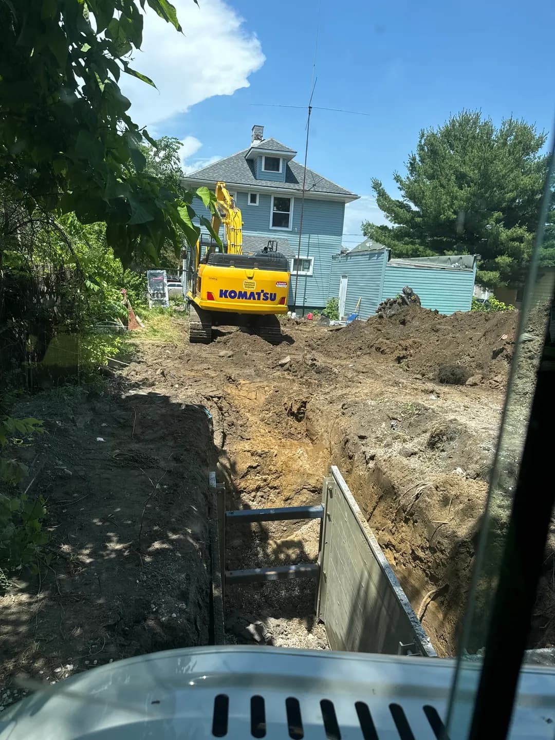 Excavator working beside a residential trench during underground sewer line repair